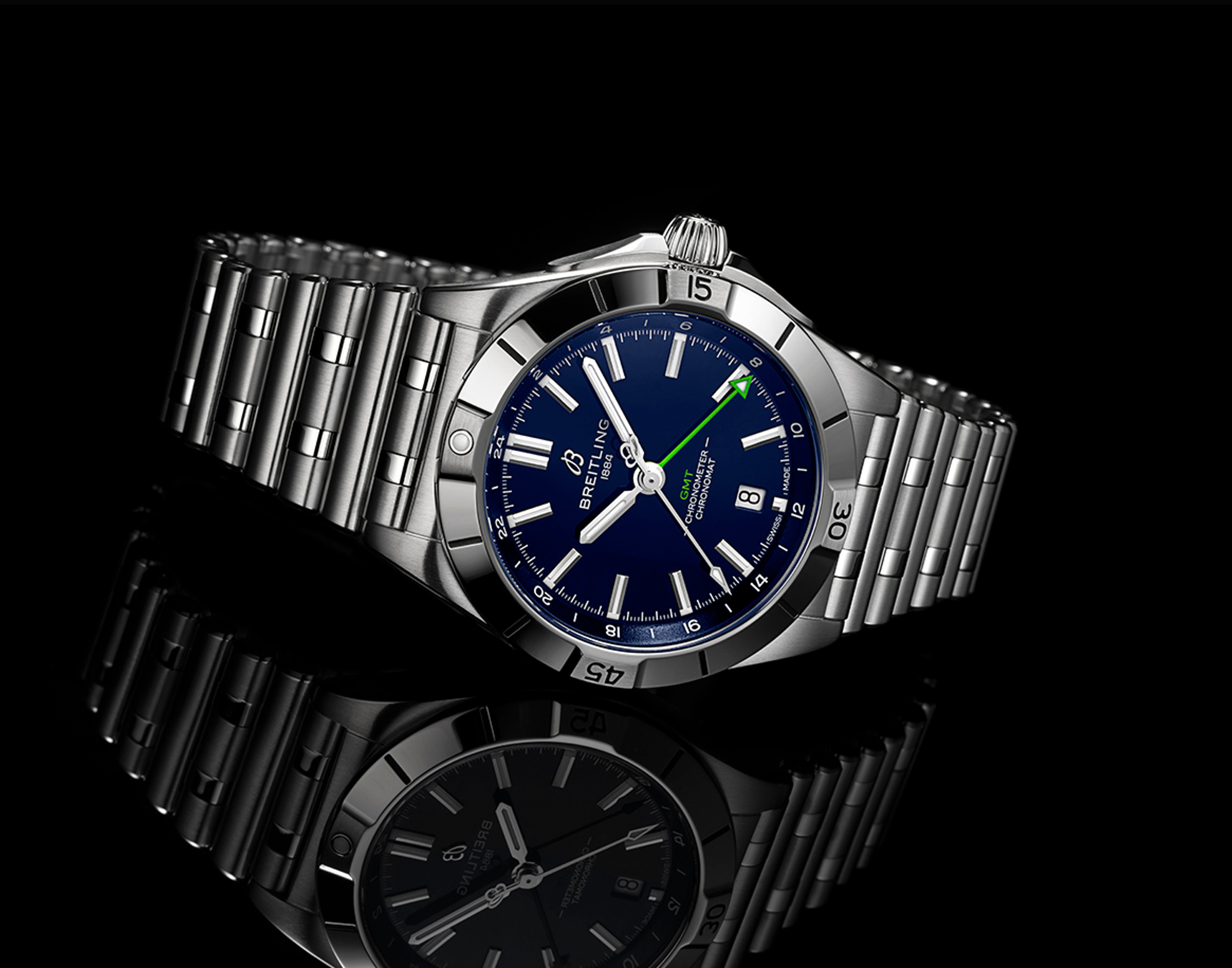 {generated} Breitling Chronomat GMT with blue dial and green GMT hand shown on polished steel bracelet against a dark reflective surface