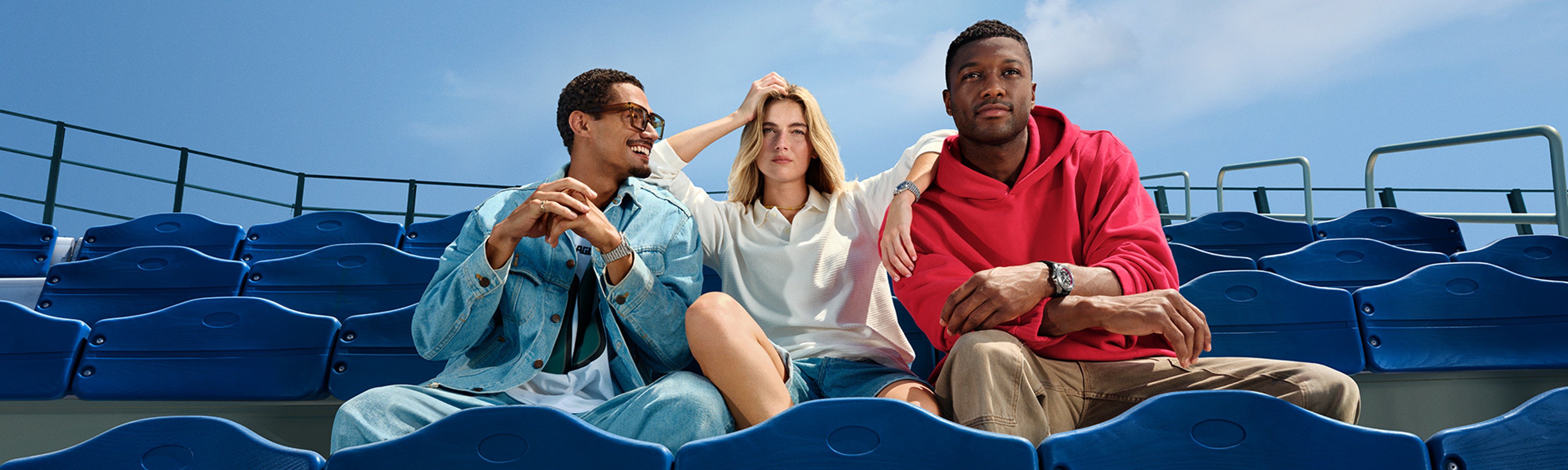 {generated} Three friends relax in bright blue stadium seats, each showcasing a Breitling watch in a casual NFL-inspired setting.