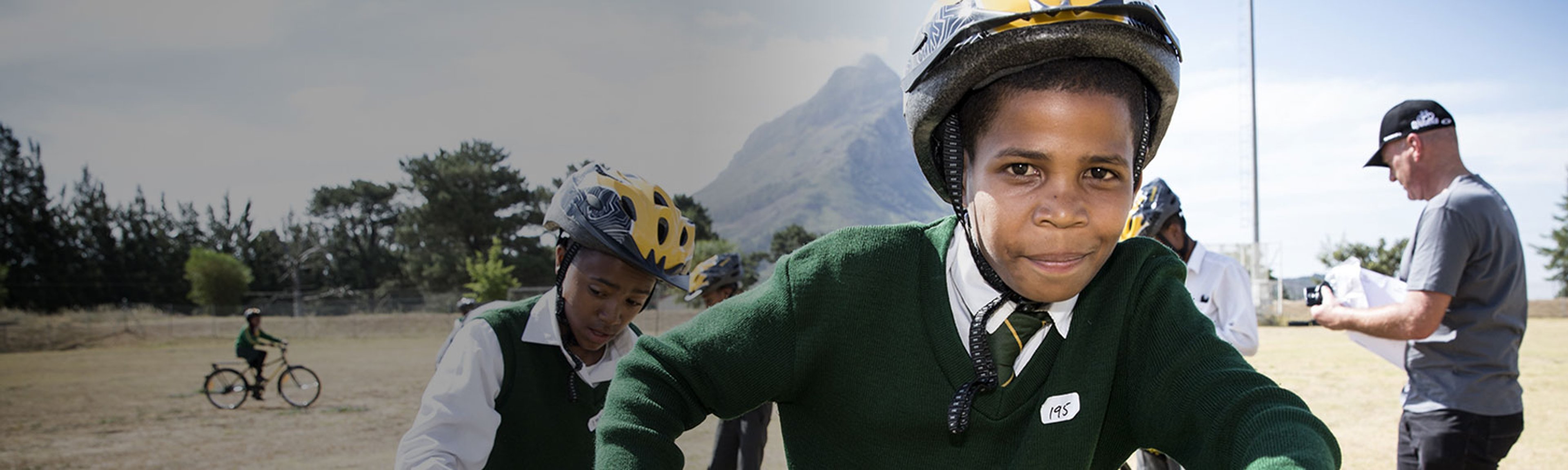 {generated} 學生佩戴頭盔在戶外騎行，在山景背景中參與Breitling x Qhubeka公益活動。