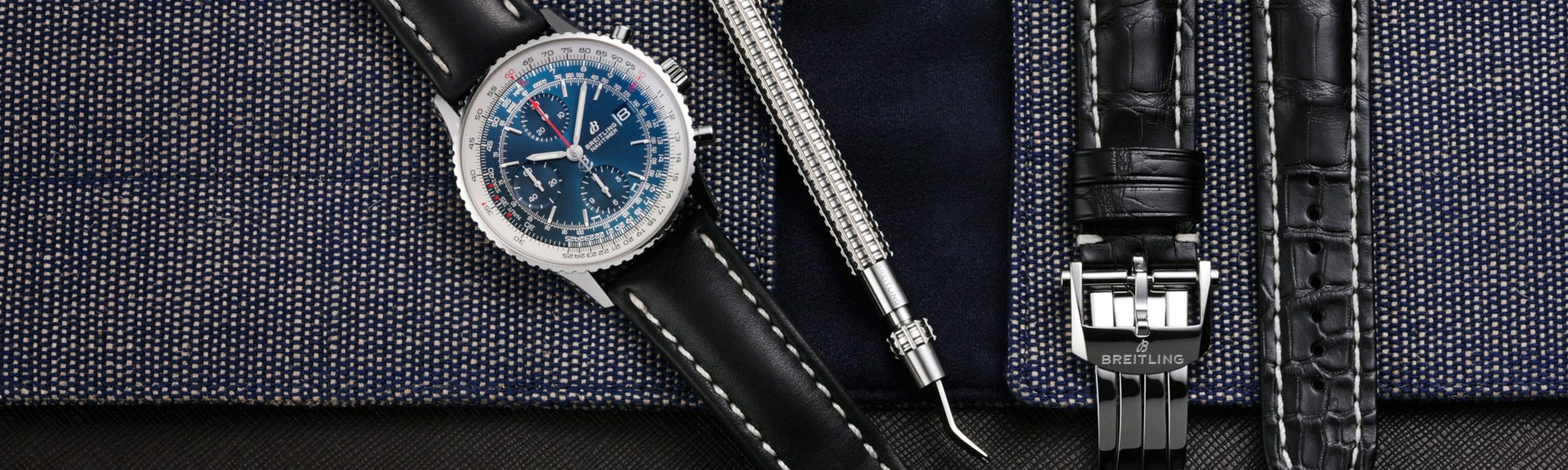 {generated} Breitling Navitimer with blue dial shown beside strap‑change tool and black leather Breitling strap on textured fabric