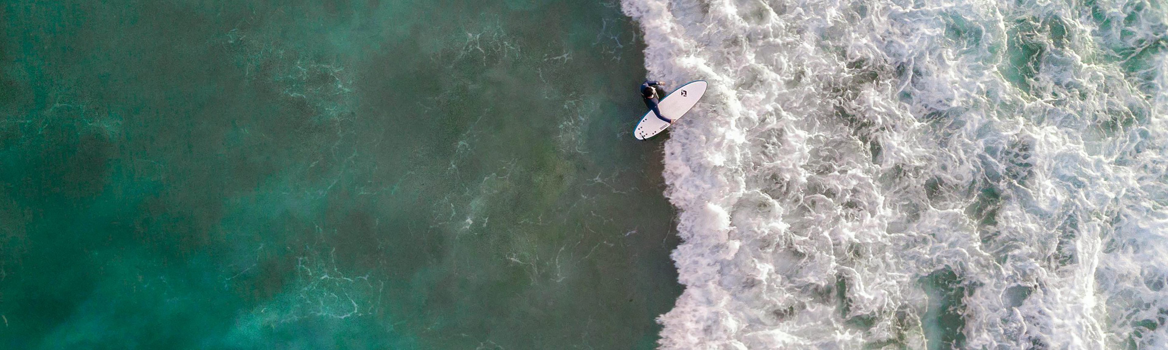 {generated} Un surfeur progresse sur des vagues écumeuses dans une mer émeraude, reflétant l’engagement de Breitling pour la durabilité marine.