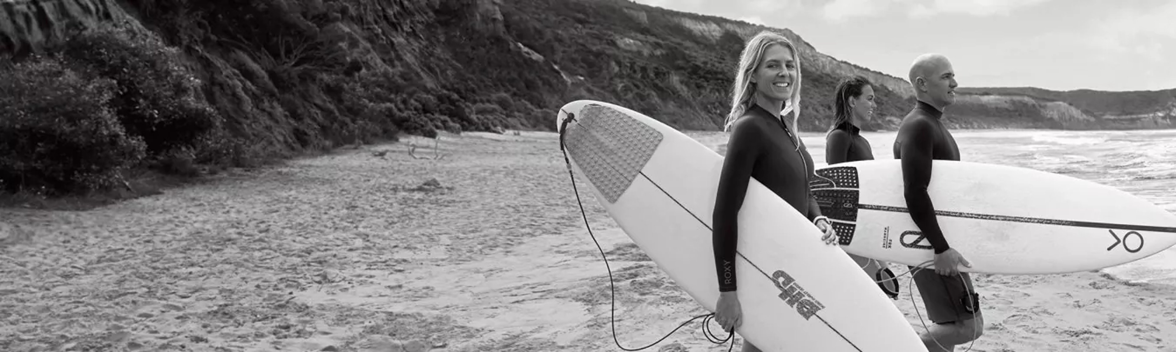 {generated} Three surfers holding boards stand on a quiet shoreline, evoking an adventurous coastal mood suited to newsletter signups.