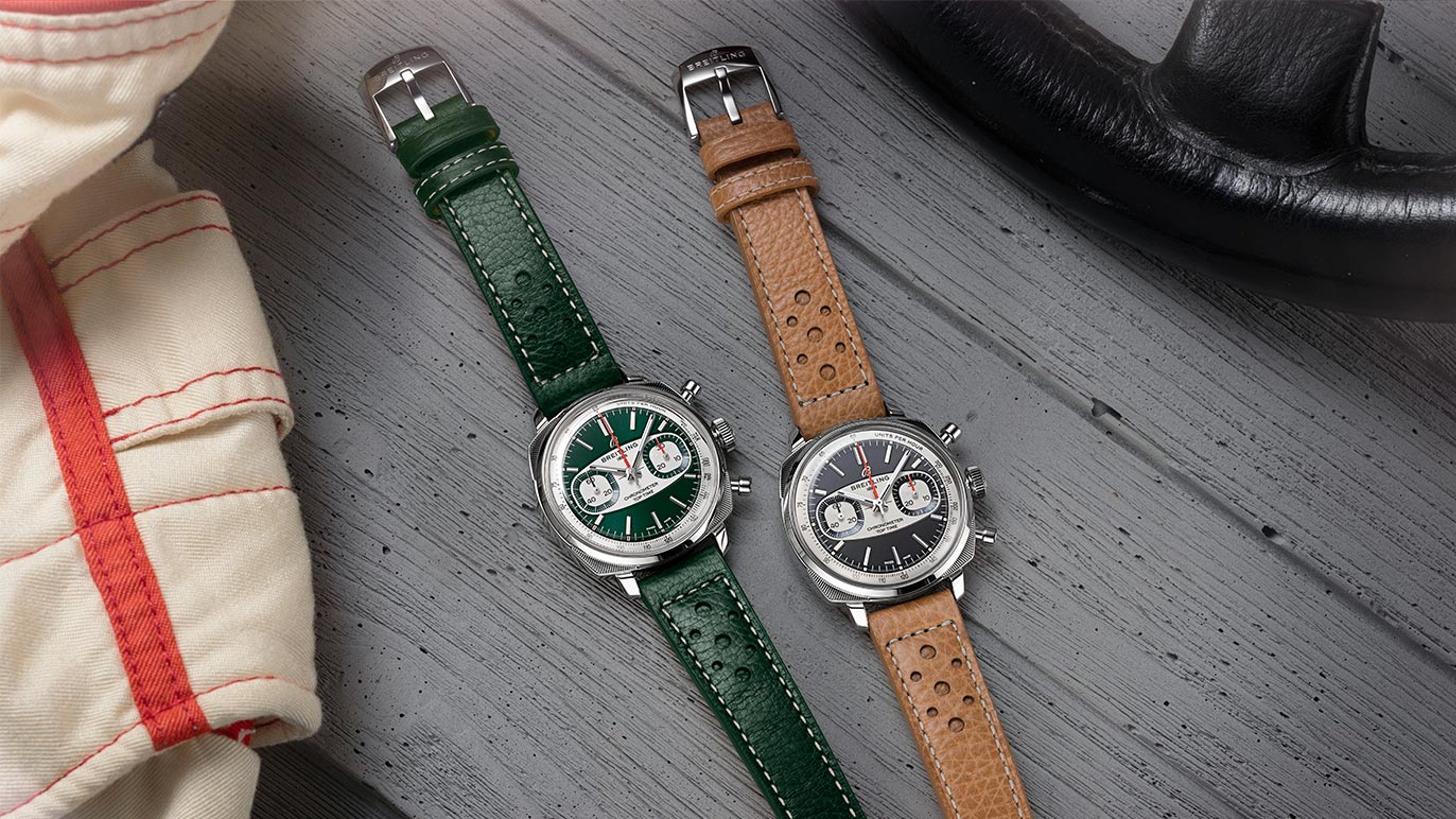 {generated} Two Breitling Top Time Racing watches with green and brown straps displayed on grey wood beside vintage racing gear