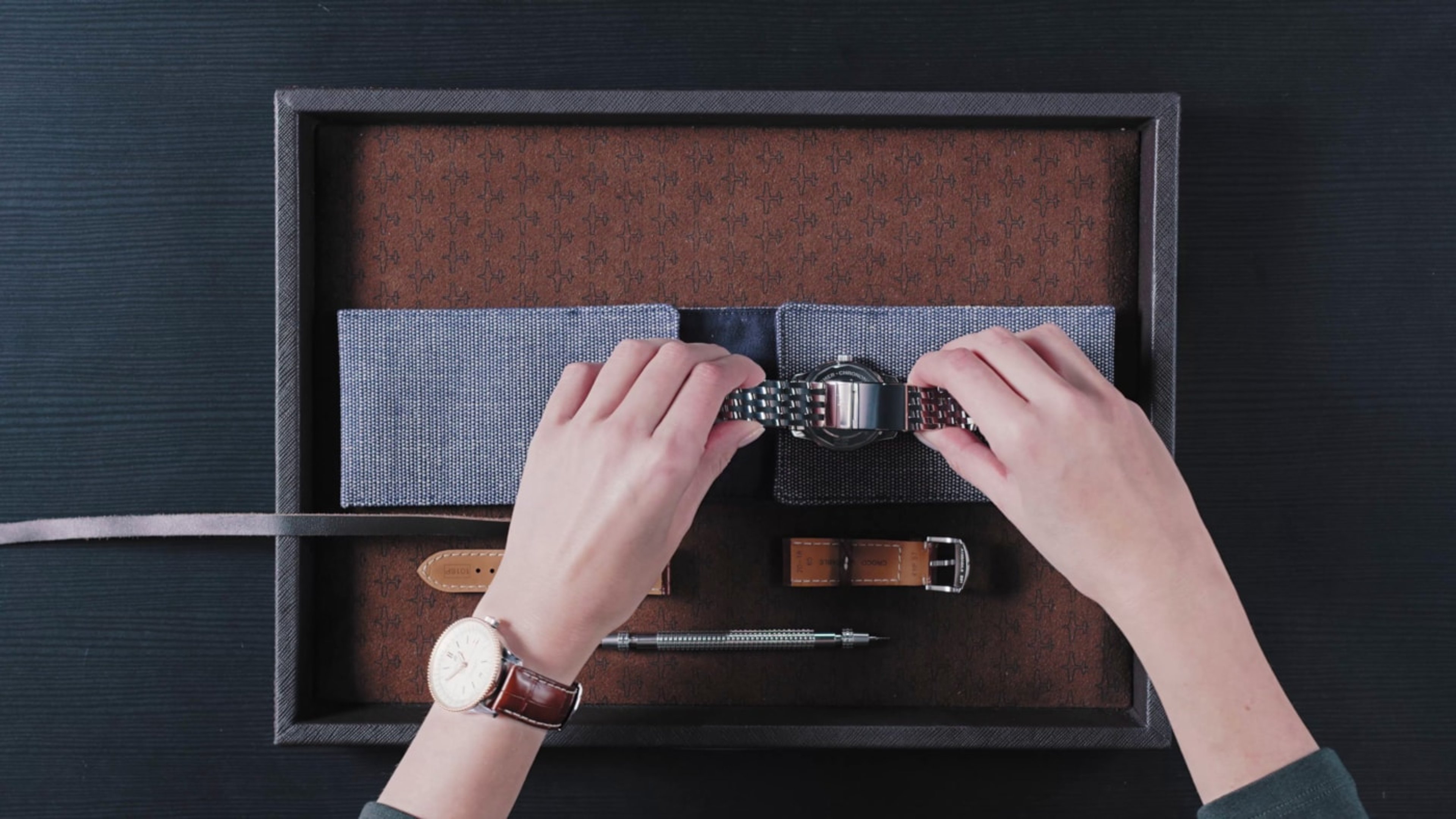 {generated} Hands adjusting a Breitling metal watch bracelet in a tray with spare leather straps and a tool for changing components