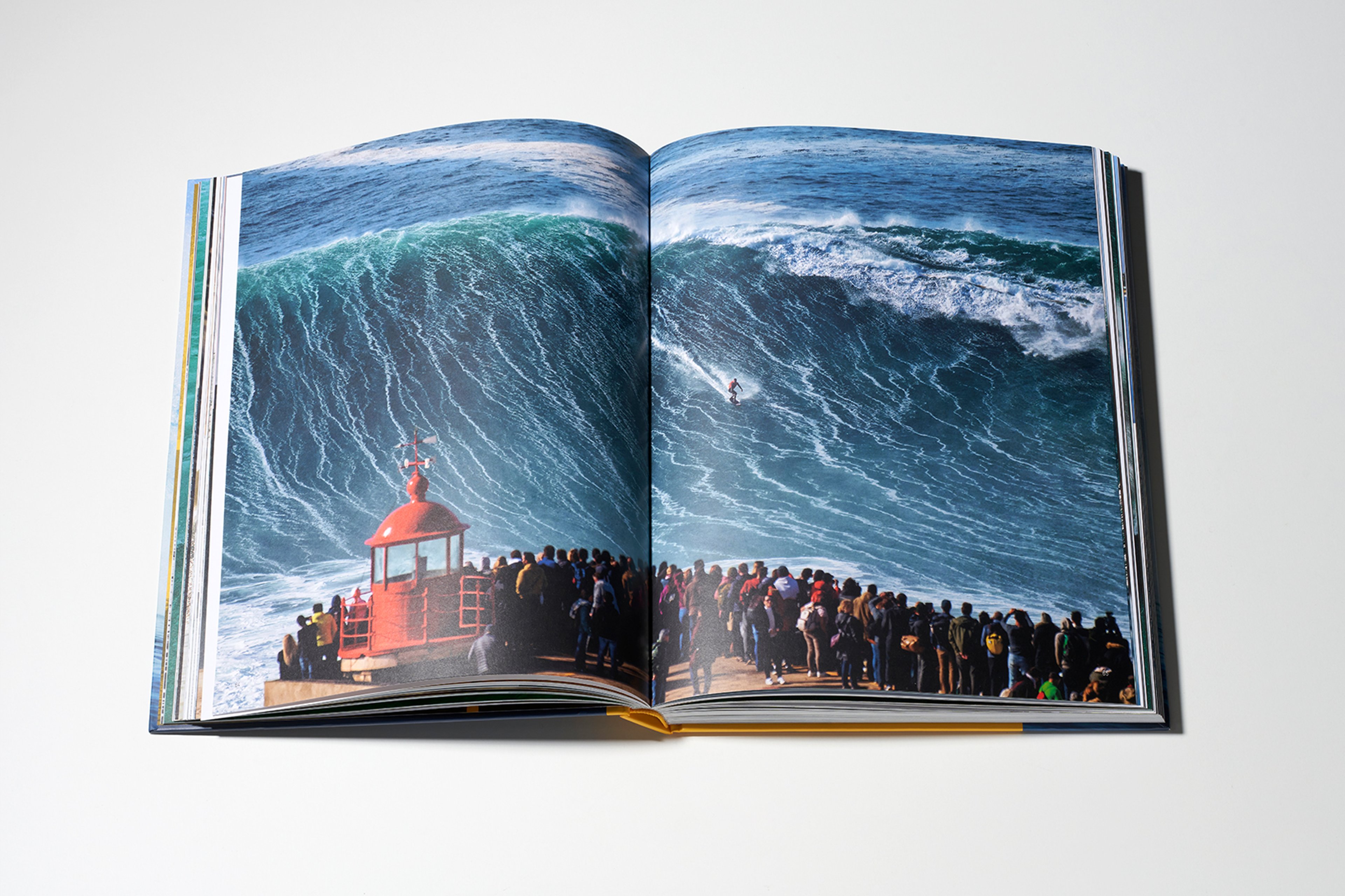 {generated} Open book showing a dramatic big‑wave surf scene with a lone surfer and a crowd gathered along a coastal lookout