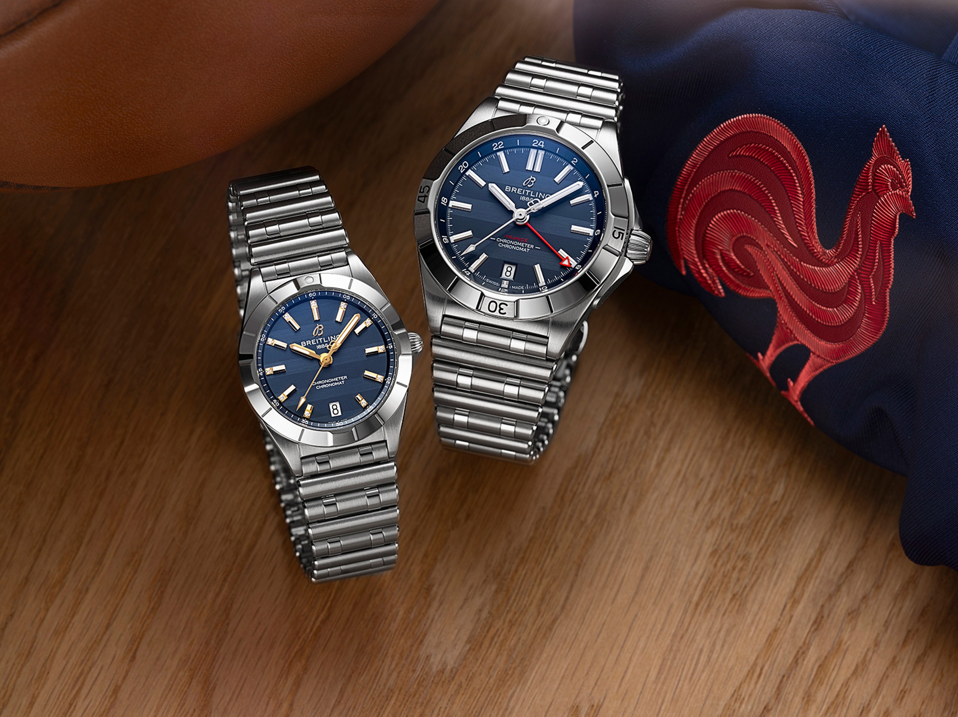 {generated} Two Breitling steel watches with blue dials set near a rugby ball and France’s red rooster emblem for Six Nations.