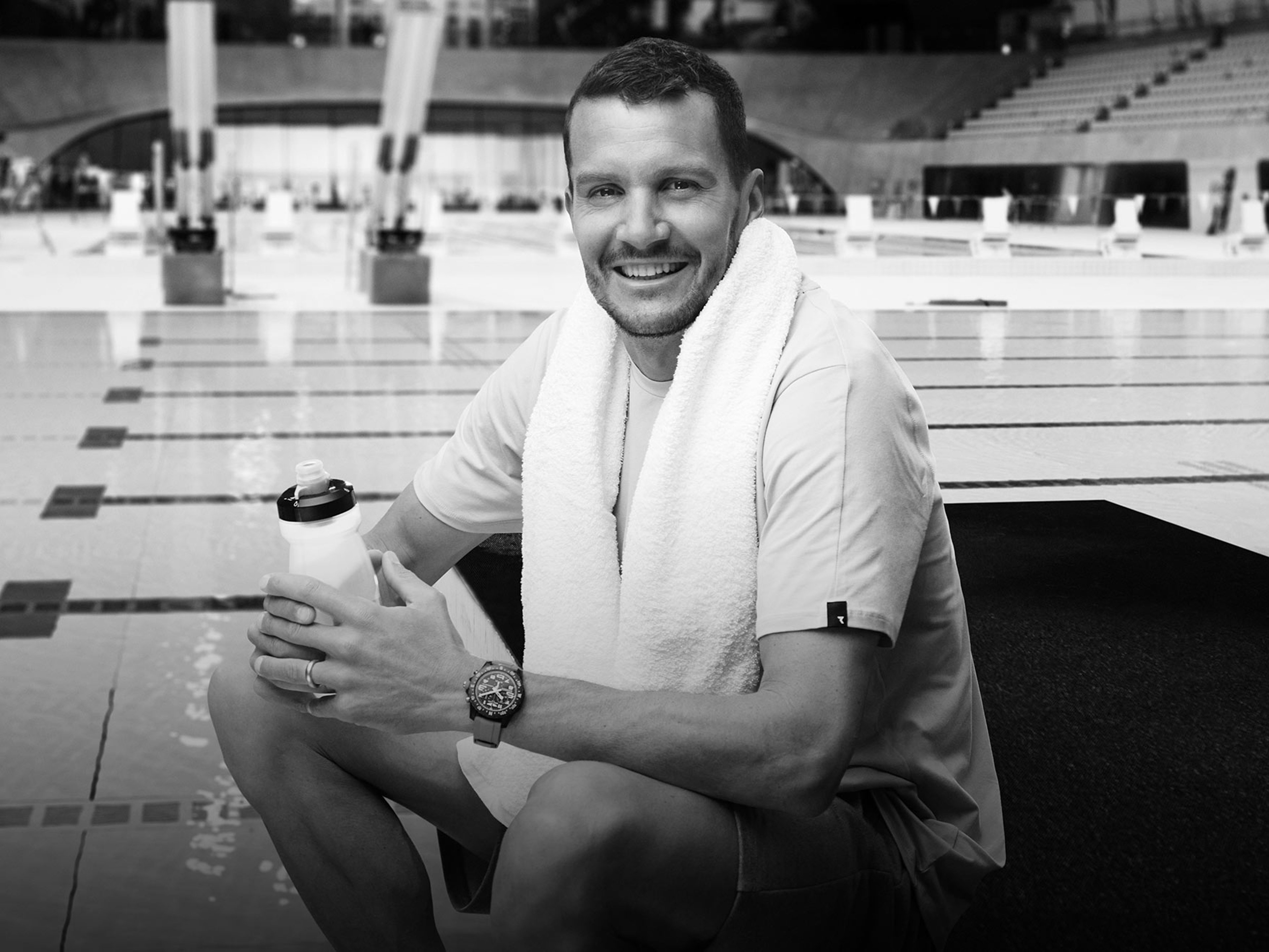 {generated} An athlete resting poolside with a towel and water bottle, wearing a Breitling sports watch in a training setting.