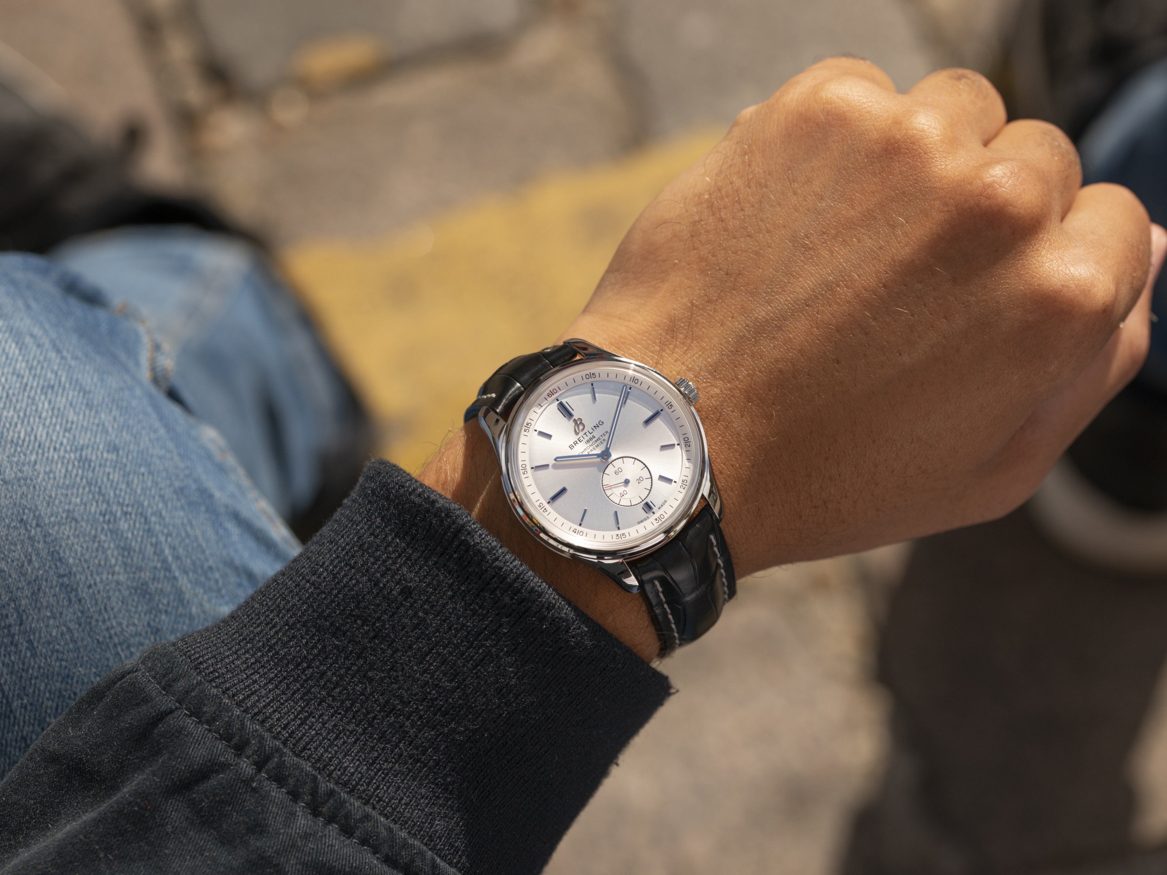 {generated} Ein Handgelenk mit einer Breitling Uhr mit silbernem Zifferblatt und schwarzem Lederband im natürlichen Straßenlicht