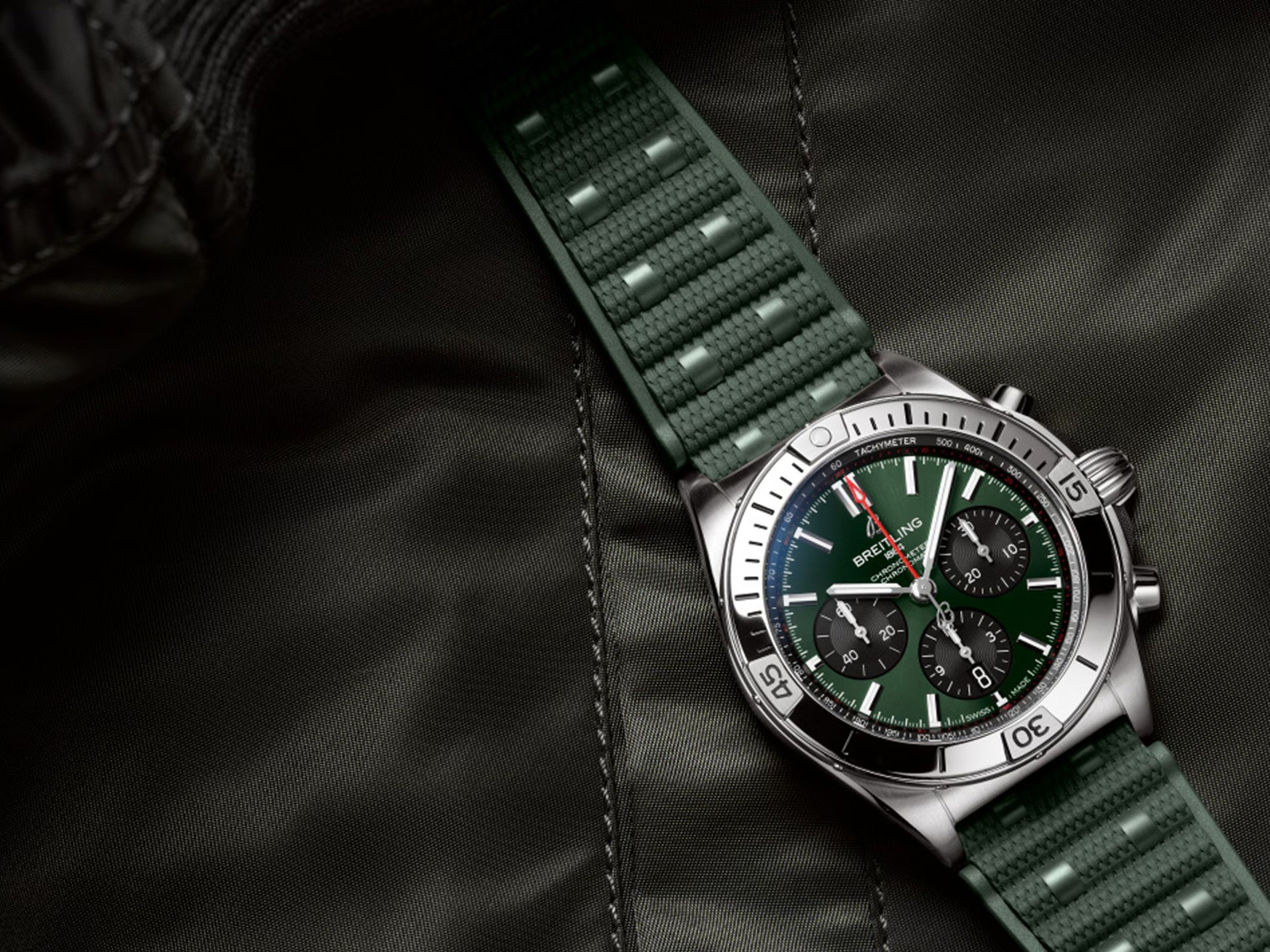 {generated} Breitling chronograph with green dial and textured green rubber strap shown in close-up on dark fabric for detail.