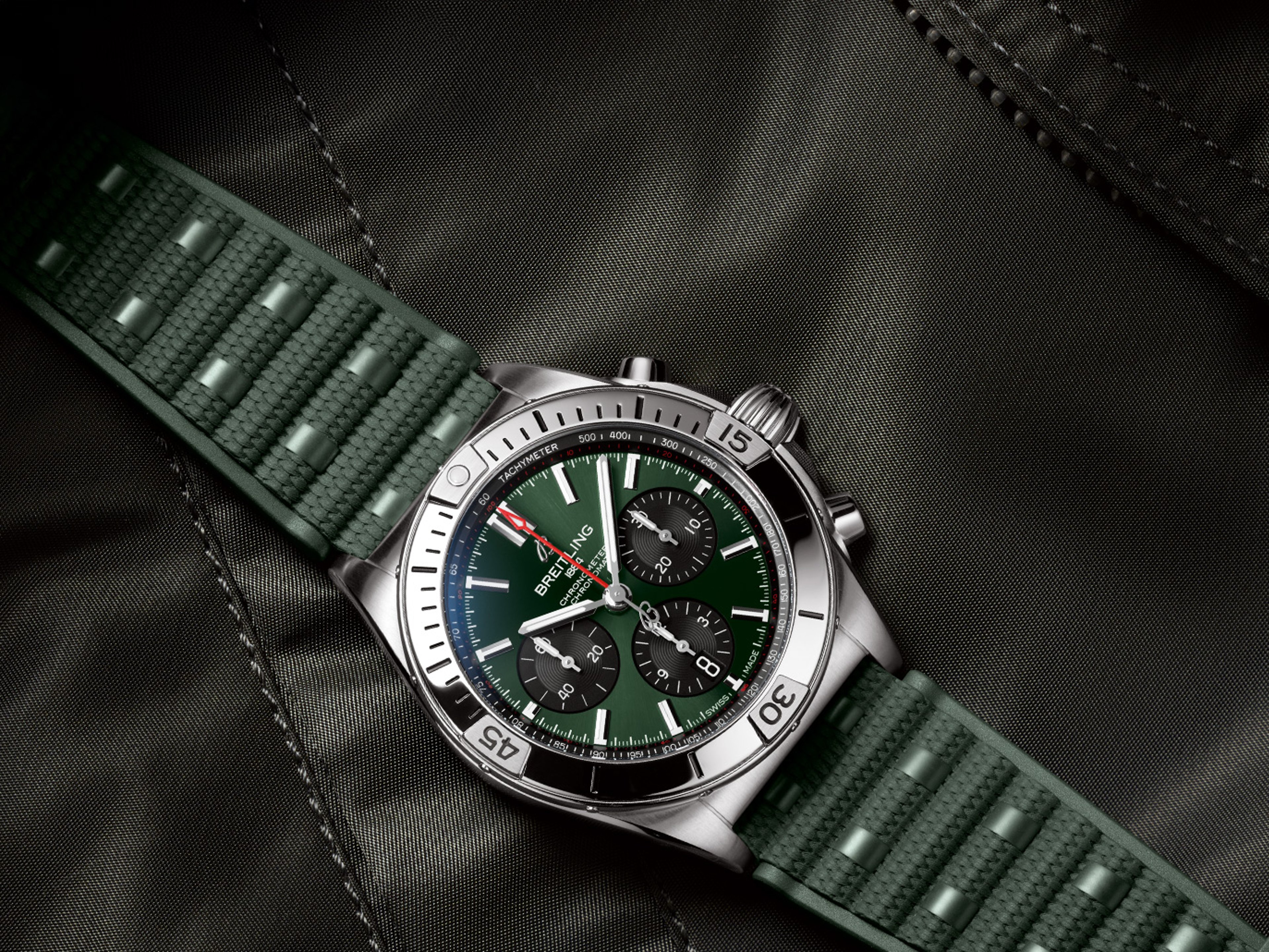 {generated} Breitling chronograph with green dial and textured green rubber strap shown in close-up on dark fabric for detail.