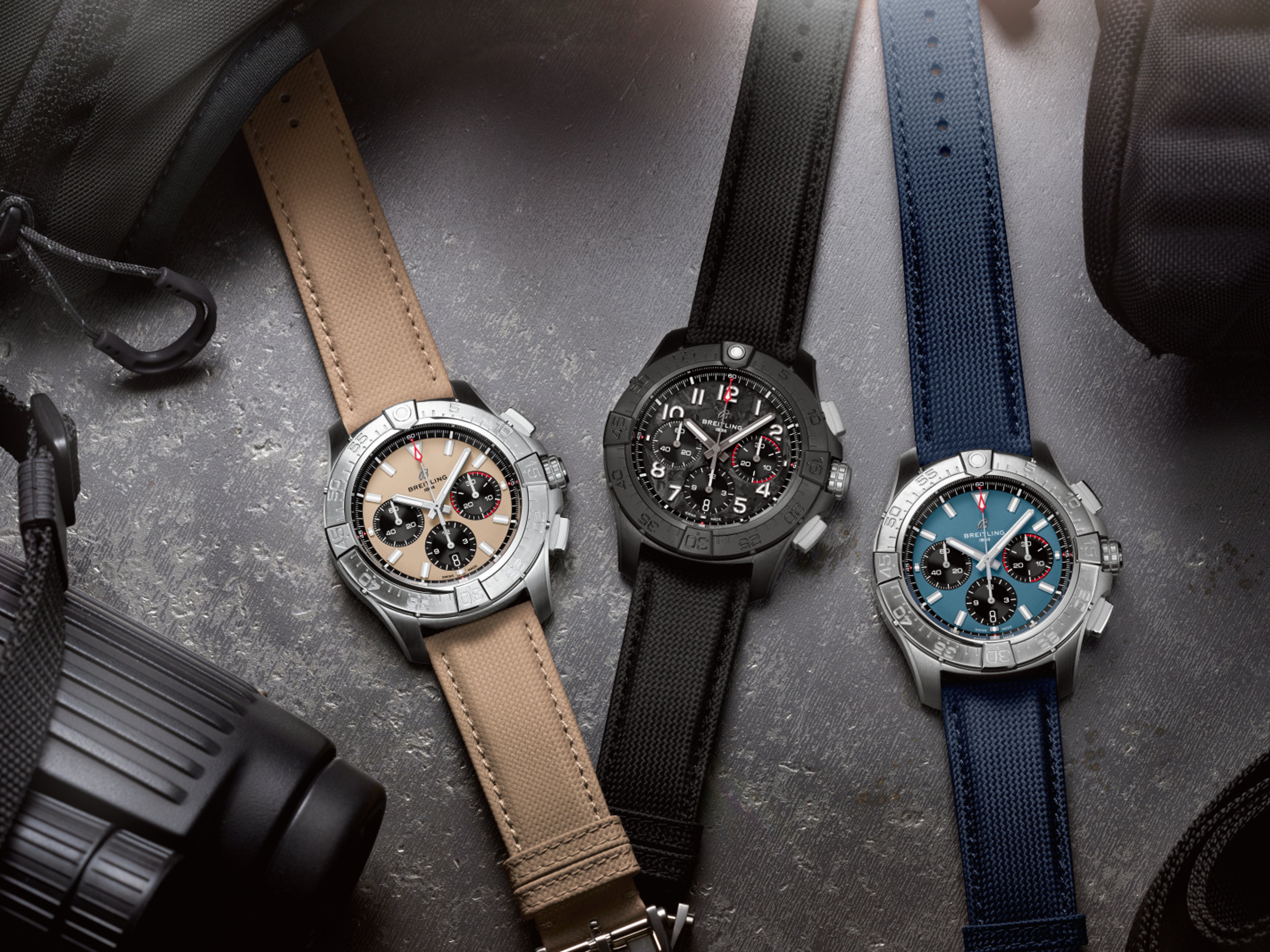 {generated} Three Breitling chronograph watches displayed with new leather straps in beige, black, and blue against a rugged backdrop.