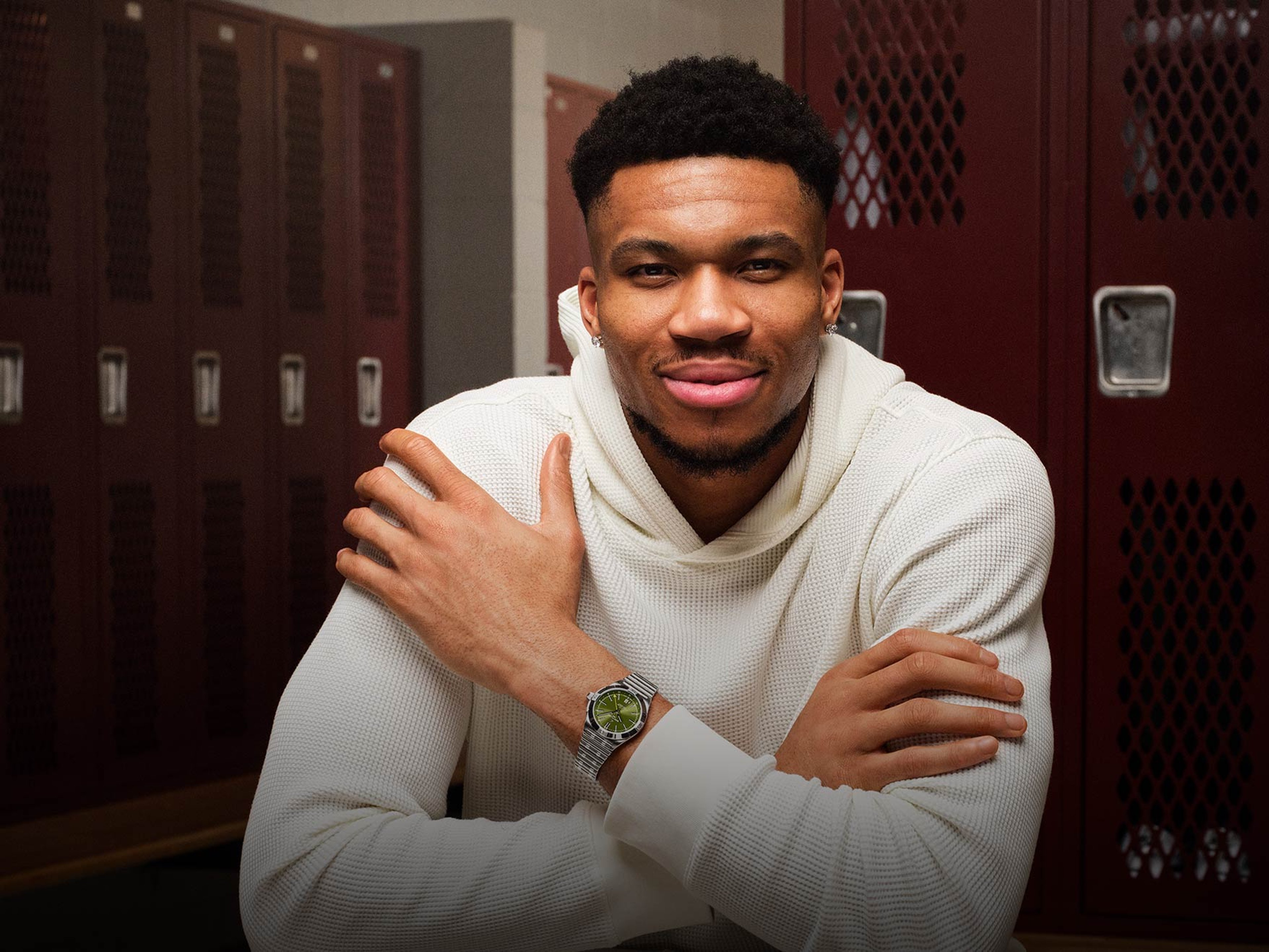 {generated} A man in a white hoodie poses in a locker room, showcasing a Breitling watch with a steel bracelet on his crossed arms.