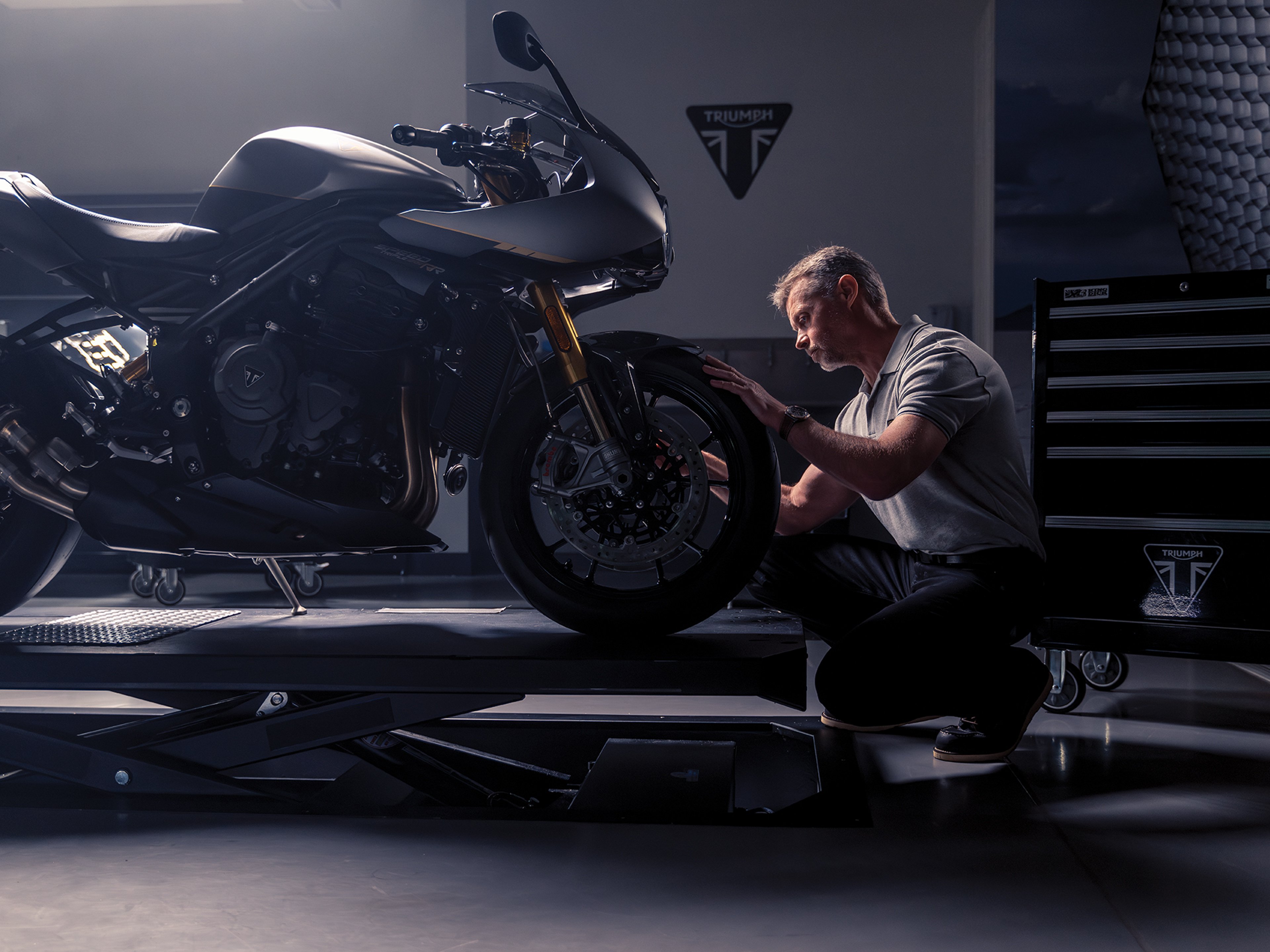 {generated} Mechanic inspecting a Triumph motorcycle’s front wheel in a dim workshop with focused light highlighting its sleek design