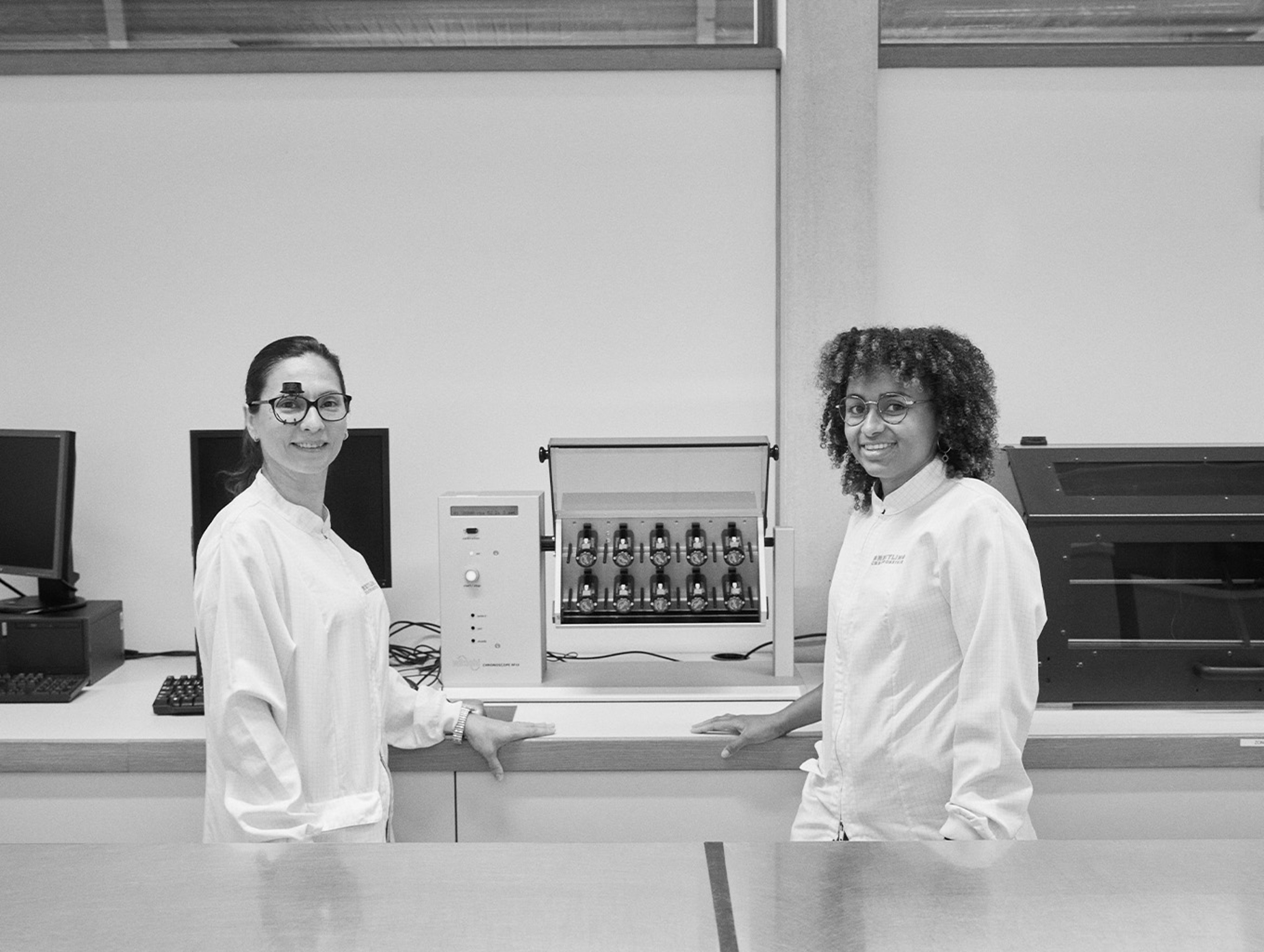 {generated} Two technicians in a Breitling lab stand beside precision testing equipment highlighting the brand’s quality and performance.