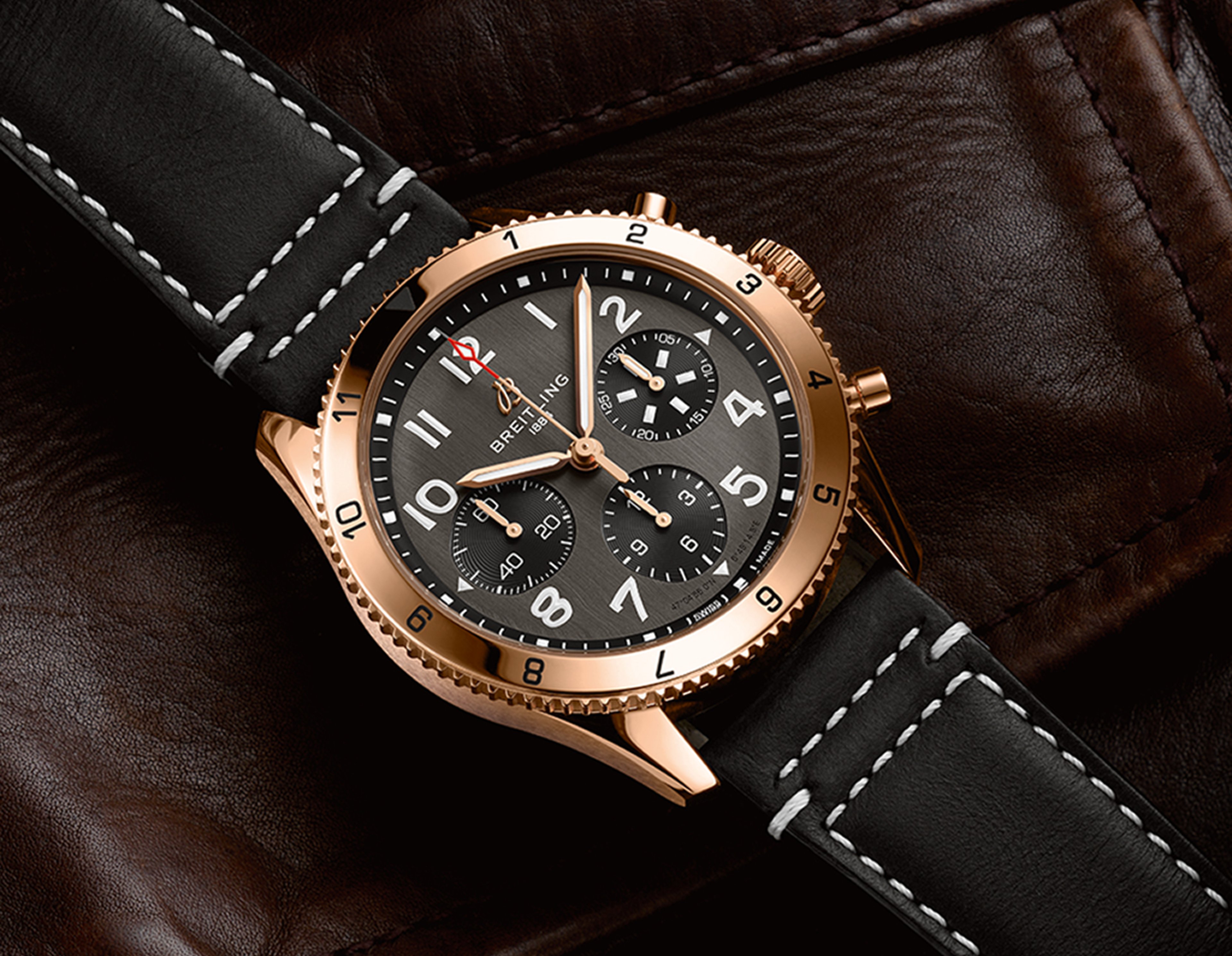 {generated} Breitling Classic Avi watch in rose gold with a black dial and leather strap displayed against textured brown leather