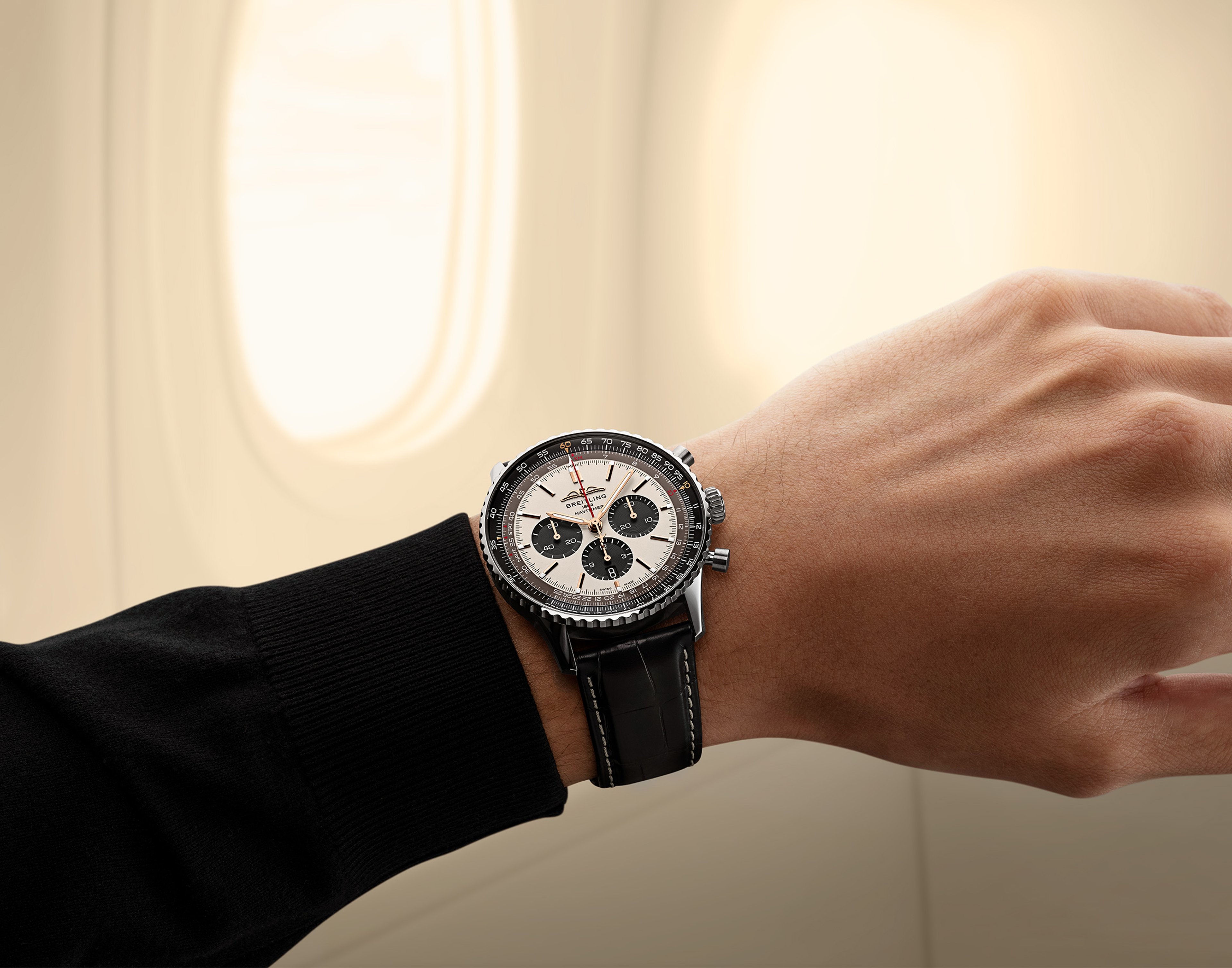 {generated} A wrist wearing a Breitling Navitimer with black leather strap shown against a softly lit aeroplane window backdrop.