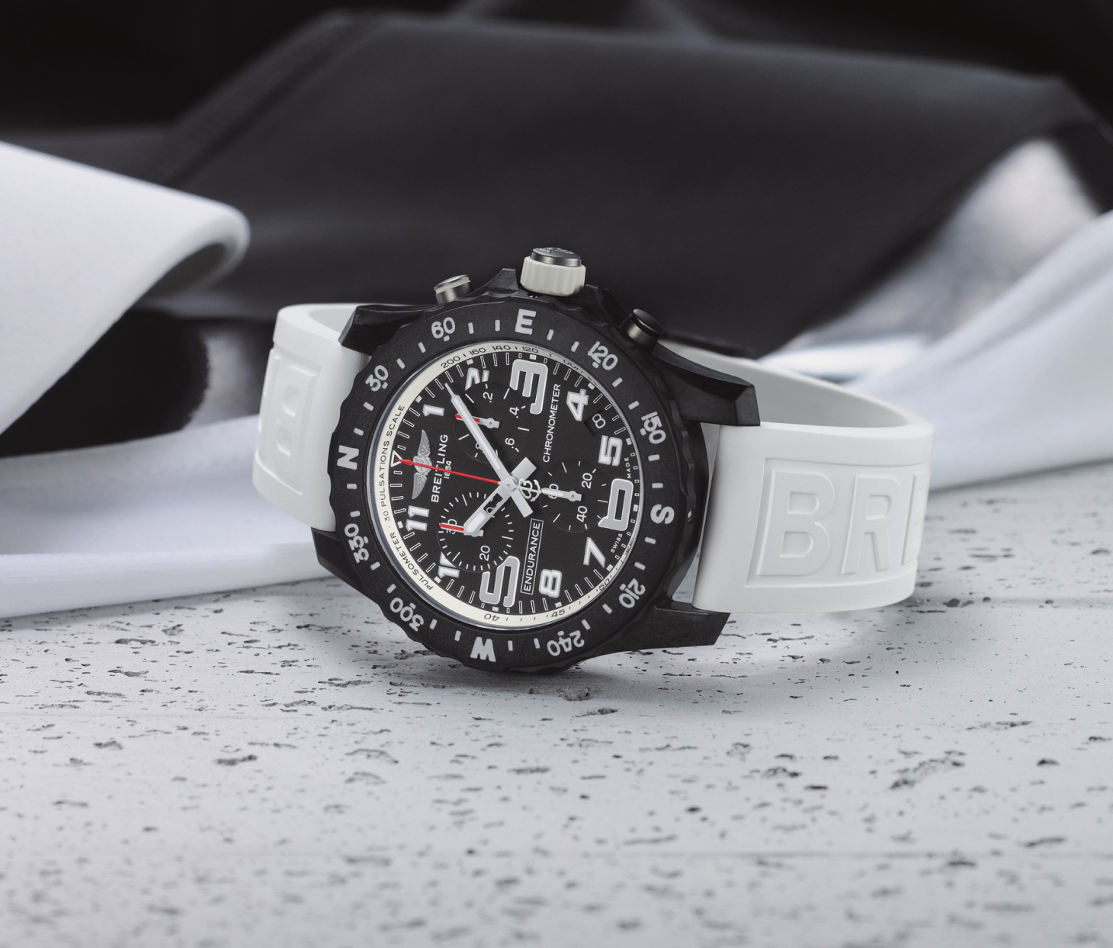 {generated} Breitling Endurance Pro,搭配黑色計時面盤與白色Breitling錶帶,置於淺色紋理表面。