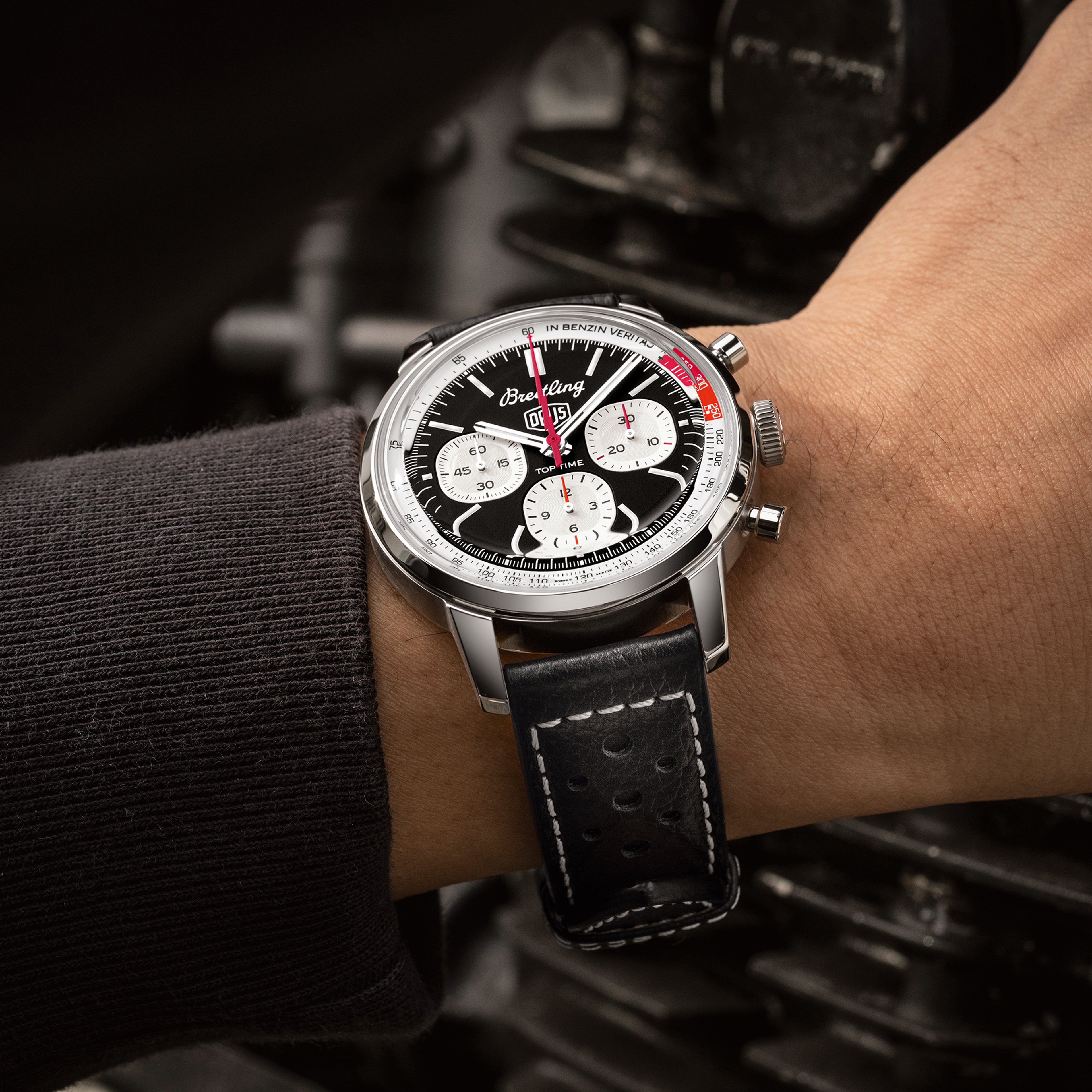 {generated} Breitling Top Time Deus watch on a wrist, highlighting its black dial, white subdials and leather strap near machinery.