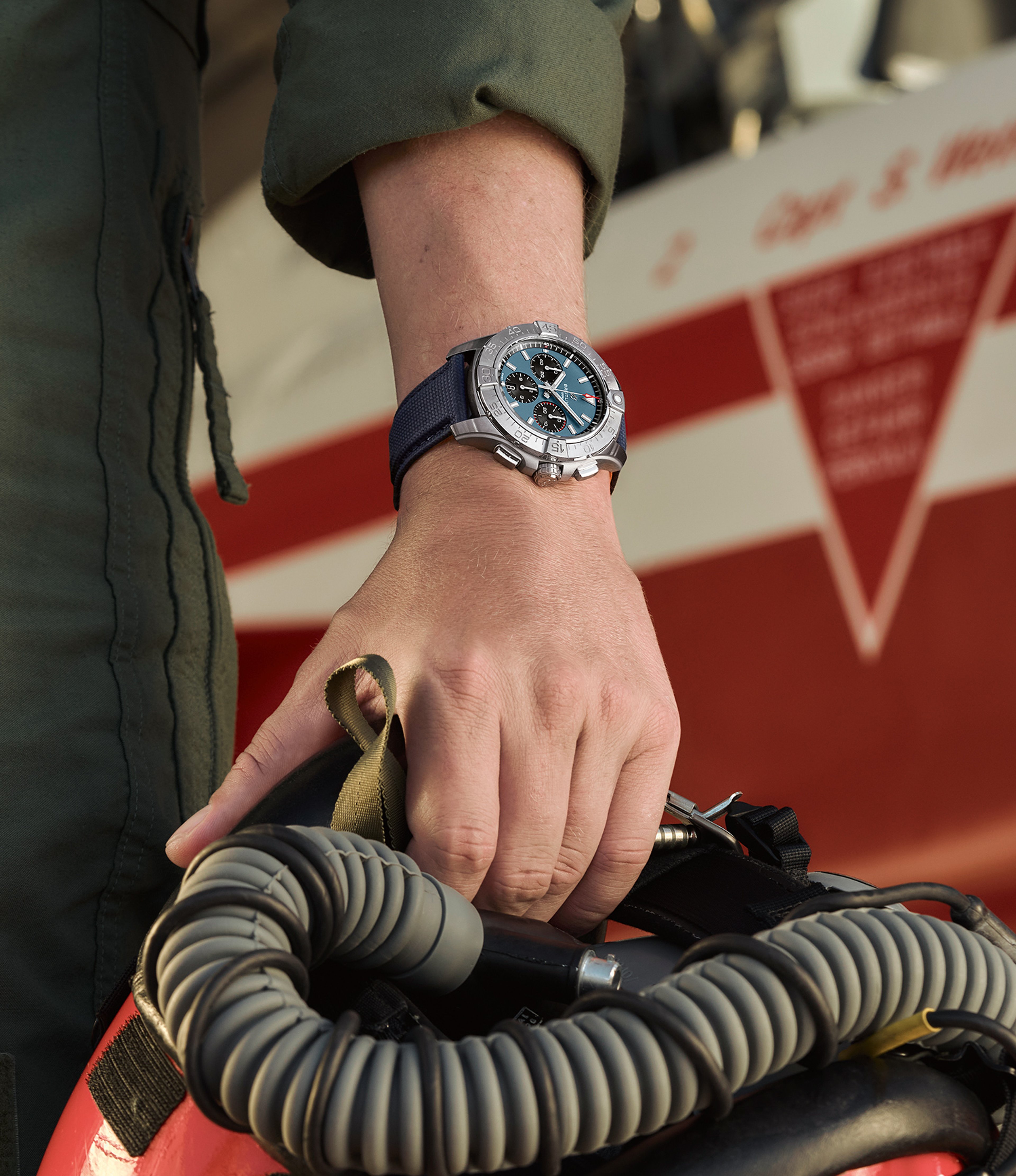 {generated} パイロットが装備を持つ手元に、青い文字盤のBreitlingクロノグラフがパトルイユ・スイス機の前で映える。