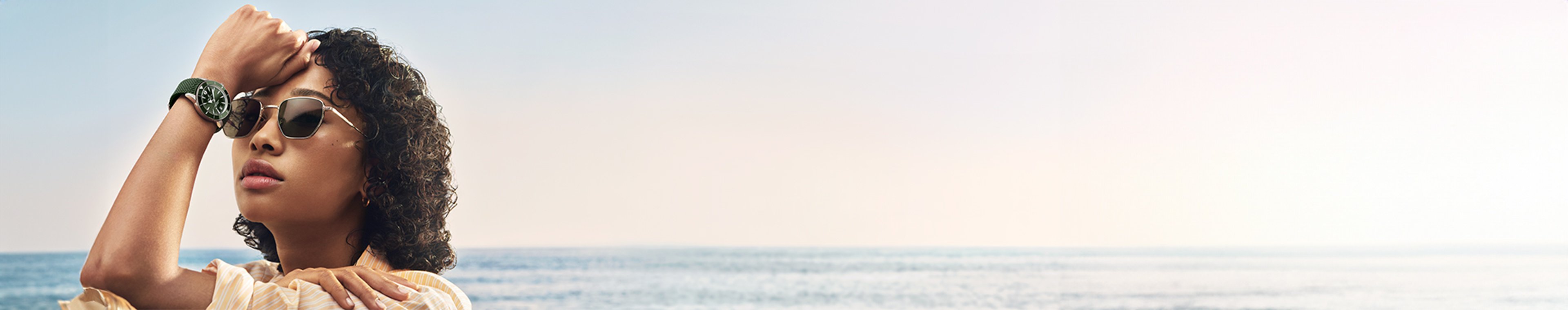 {generated} A person by the sea raises an arm, showcasing a green‑strap Breitling watch against a calm horizon in soft sunlight.