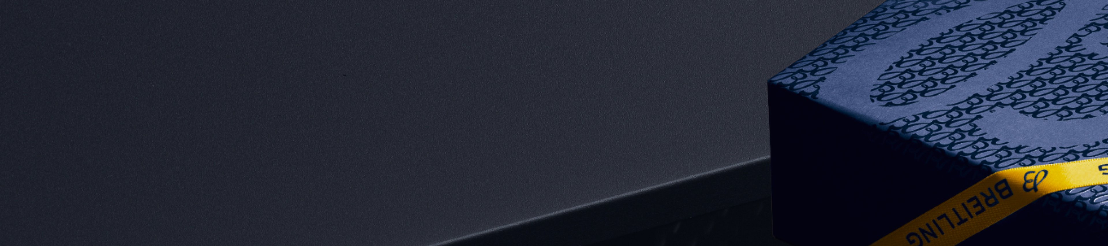 {generated} A dark setting featuring a blue Breitling gift box with signature pattern and yellow Breitling ribbon accent.